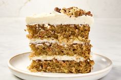 a slice of carrot cake with white frosting and pecans in the middle on a plate