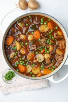 a pot filled with meat and vegetables on top of a white table next to potatoes