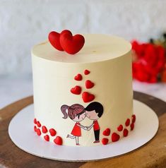 a white cake decorated with red hearts and two people kissing on the top, sitting on a wooden platter