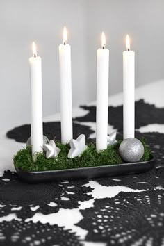 four white candles sitting on top of a tray filled with green grass and silver balls