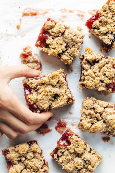 someone is holding their hand over some desserts that are on a white surface with crumbs all around them