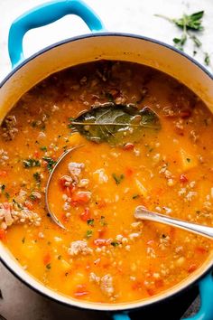 a blue pot filled with soup on top of a stove next to a wooden spoon