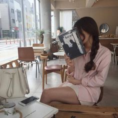 a woman sitting in a chair holding up a book over her face while looking at the camera