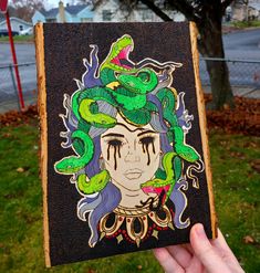 a hand holding up a drawing of a woman with snakes on her head