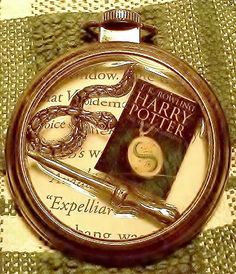 a harry potter pocket watch with an image of a wand and book on the cover