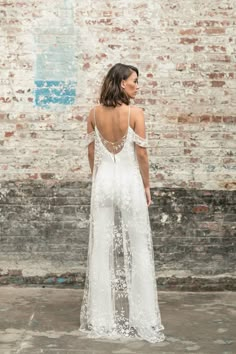 a woman standing in front of a brick wall wearing a white dress with open back