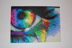 a cross - stitch photo of a rainbow colored eye is hanging on the white wall