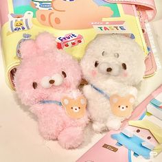 two stuffed animals sitting next to each other on top of a pink and white book