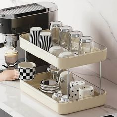 a coffee maker with cups and saucers in it on a kitchen counter next to a toaster