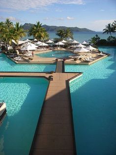 an outdoor swimming pool with lounge chairs and umbrellas next to the water, surrounded by palm trees