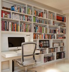 a computer desk sitting in front of a bookshelf filled with lots of books