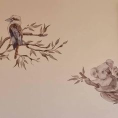 a bird sitting on top of a tree branch next to a wall with flowers painted on it