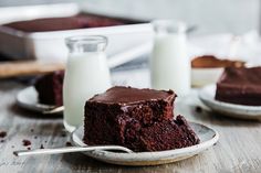 a piece of chocolate cake sitting on top of a plate next to two glasses of milk