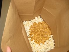 a person holding a brown paper bag filled with rice and peanut butter mixture in it