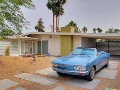 a blue car is parked in front of a house with palm trees on the side