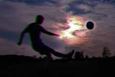 a man kicking a soccer ball on top of a grass covered field at sunset with the sun in the background