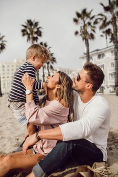 a man, woman and child sitting on the beach with palm trees in the background