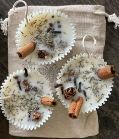 two cups filled with different types of spices on top of a cloth bag next to cinnamons and cloves