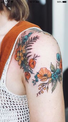 a woman's arm with flowers on it and an orange vest underneath her sleeve