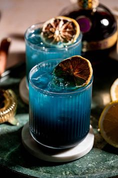 two glasses filled with blue liquid sitting on top of a table next to lemons