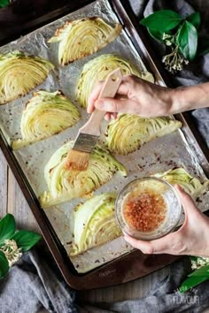 someone is cutting up cabbage on a baking sheet with a spatula and seasoning