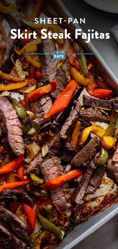 a sheet pan filled with steak and peppers on top of a table next to other food