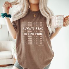 a woman with blonde hair holding a coffee mug and wearing a t - shirt that reads always read the fine print