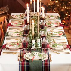 a table set for christmas dinner with candles on the top and place settings in front