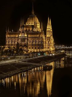 the building is lit up at night with lights on it's sides and reflecting in the water