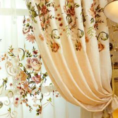 the curtains are hanging in front of the window with floral designs on them, along with a table and chair