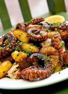 a white plate topped with meat and potatoes covered in seasoning next to a slice of lemon