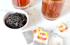 two cups of tea sit next to each other on a marble counter top, with one cup filled with black tea