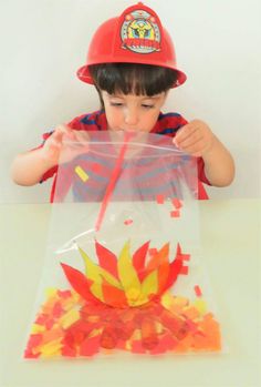 a young boy wearing a fireman's hat and holding a plastic bag filled with autumn leaves