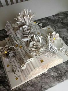 an open book with paper flowers and butterflies on the pages, sitting on top of a table