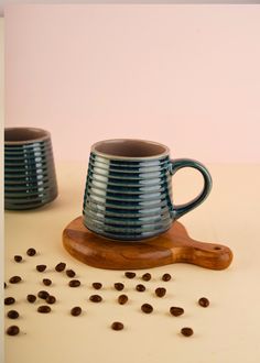 two coffee mugs sitting on top of a wooden board next to some coffee beans