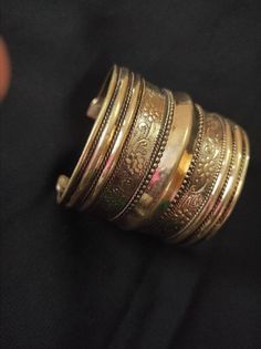 a stack of gold bracelets sitting on top of a black cloth next to a person's hand