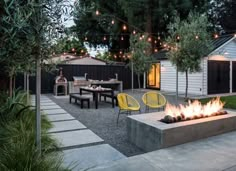 a fire pit in the middle of a backyard with lights strung over it and chairs around it