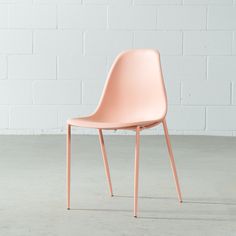 a pink chair sitting in front of a white brick wall with the seat up on it's side