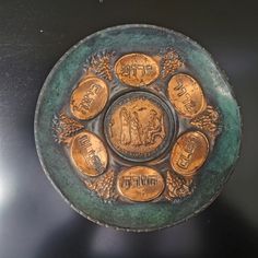 a metal plate with some gold coins in it on a black table top and two other items around the edge