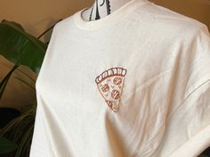 a white t - shirt with a slice of pizza embroidered on it