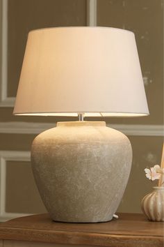 a white lamp sitting on top of a wooden table next to a vase with flowers