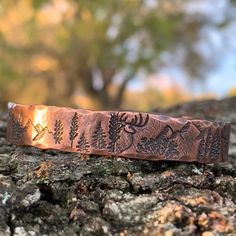 a close up of a piece of metal with trees and leaves engraved on the side