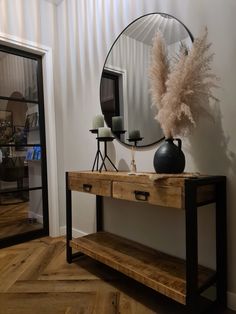 a wooden table with a mirror and vase on it next to a wall mounted shelf