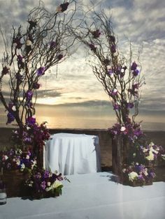 an outdoor ceremony setup with flowers and branches on the ground, overlooking the ocean at sunset