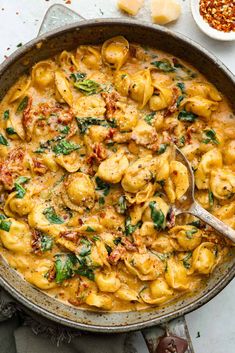 a skillet filled with pasta and spinach on top of a white countertop