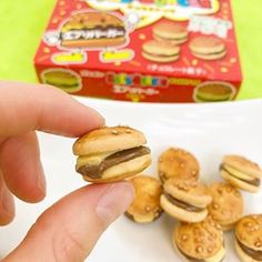 a hand holding a mini hamburger in front of small burgers on a white plate