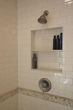 a bathroom with white tile and shelves on the wall above the shower head, along with soap dispensers