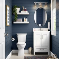 a white toilet sitting next to a bathroom sink under a round mirror on a wall