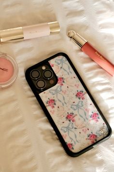 an iphone case sitting on top of a bed next to lipstick and other makeup products