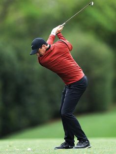 a man in red shirt and black pants swinging a golf club at a green course